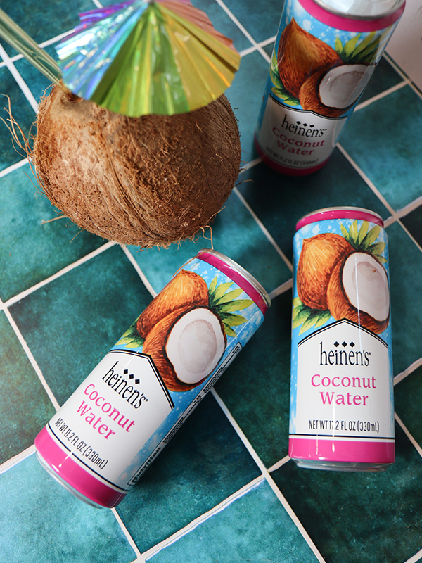 Cans of Heinen's Coconut Water Beside a Coconut with an Umbrella