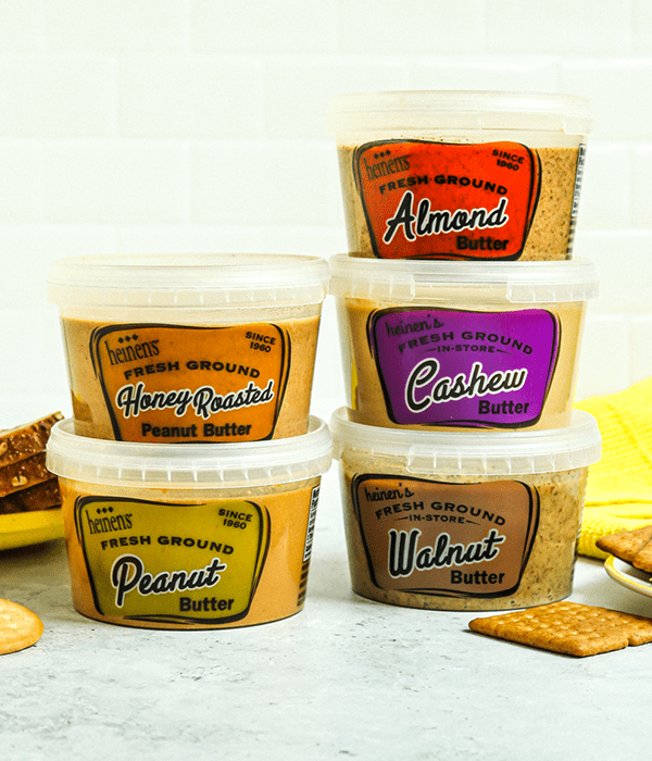 Five Plastic Containers of Heinen's Fan Favorite Fresh Ground Nut Butters Arranged in Stacks