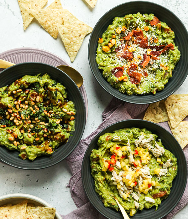 Vertical Image of Fresh Guacamole in Serving Bowls with Various Topping and Tortilla Chips