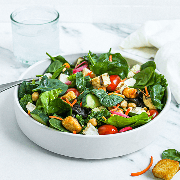 A Serving Bowl Filled with a Green Salad. Served with a Glass if Water.