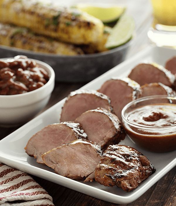 Grilled BBQ Pork Tenderloin on a plate with street corn in the background