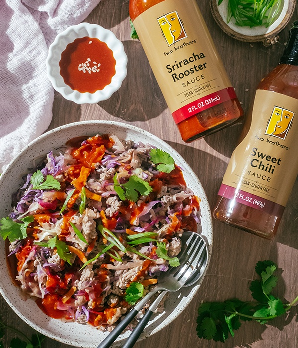 Overhead view of Egg Roll in a Bowl, beside bottles of Two Brothers Sweet Chili sauce and Two Brothers Sriracha Rooster sauce 