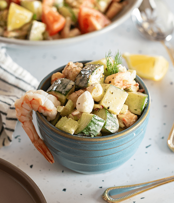 Cold Citrus Shrimp Salad in a Small Blue Bowl with a Full Piece of Shrimp Hanging Over the Side