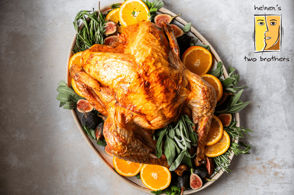 A Whole Cooked Golden Brown Turkey on a Serving Platter on Top of a Bed of Greens, Herbs and Orange Slices