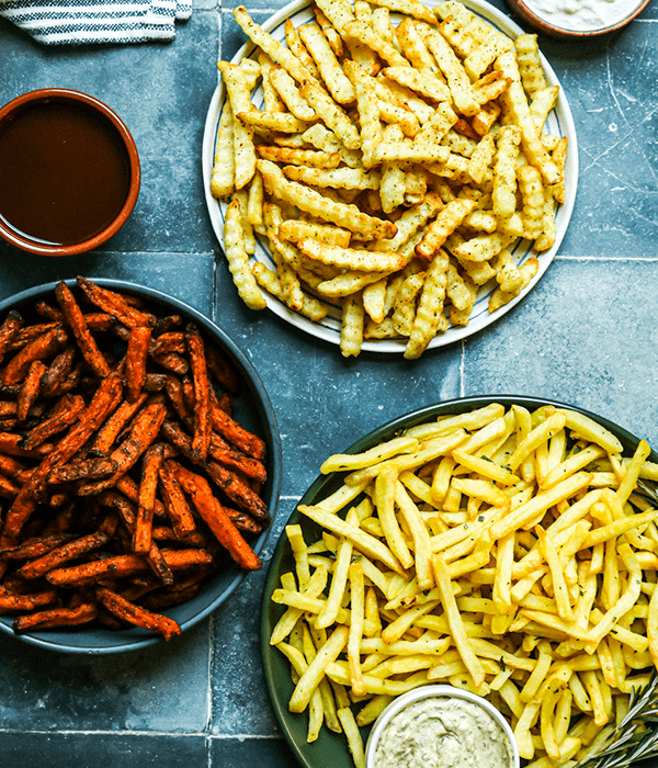 Greek Fries, Rosemary Fries and BBQ Sweet Potato Fries on Plates on a Blue Surface