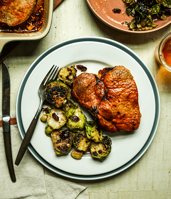 Heinen's Maple Brined Bone-In Pork Chop and Heinen's Brussels Sprouts with Hazelnuts and Cranberries on a Plate with a Fork