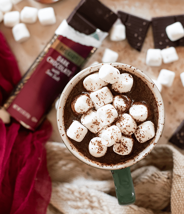 A Birds-Eye Image of Boozy Hot Chocolate with Mini Marshmallows and an Unwrapped Two Brothers Dark Chocolate Bar