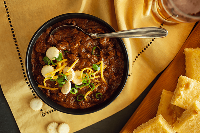 Bowl of Texas Red Chili with oyster crackers and cheese, with a side of cornbread.