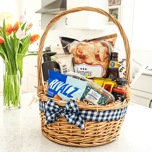 A Wicker Basket with a Handle and Blue Ribbon Filled with Various Food, Snacks and Self Care Items