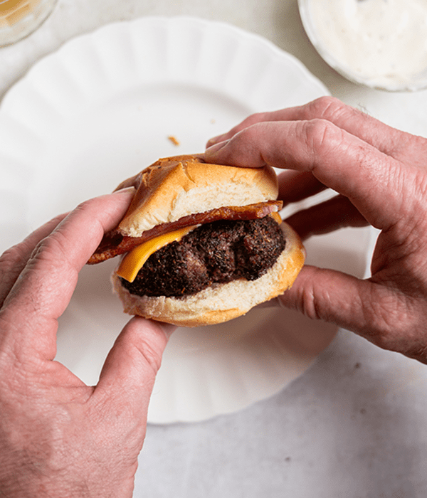 Two Hands Holding a Cheeseburger Slider