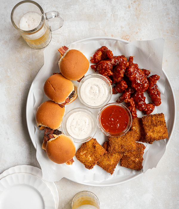 A Bird's Eye Image of a Copycat Triple Dipper Appetizer Platter Featuring Chicken Fingers, Cheeseburger Sliders, and Fried Mozzarella with Dipping Sauces