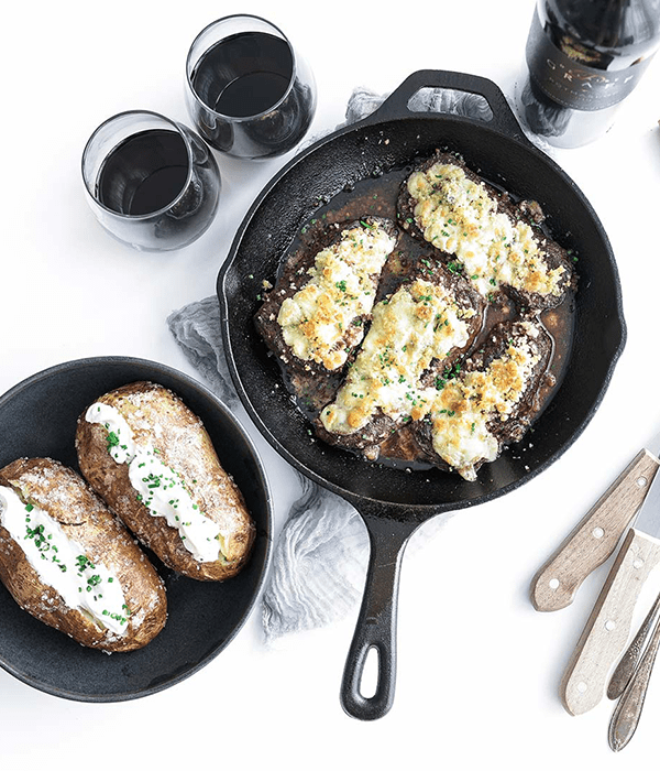 Gorgonzola Crusted Steak in a Cast Iron Skillet Beside Two Loaded Baked Potatoes