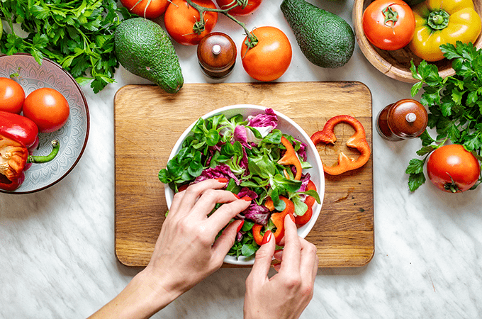 Two Hands Placing Vegetables on a Salad