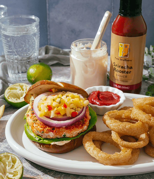 Tropical Salmon Burger served with onion rings and siracha rooster sauce. 