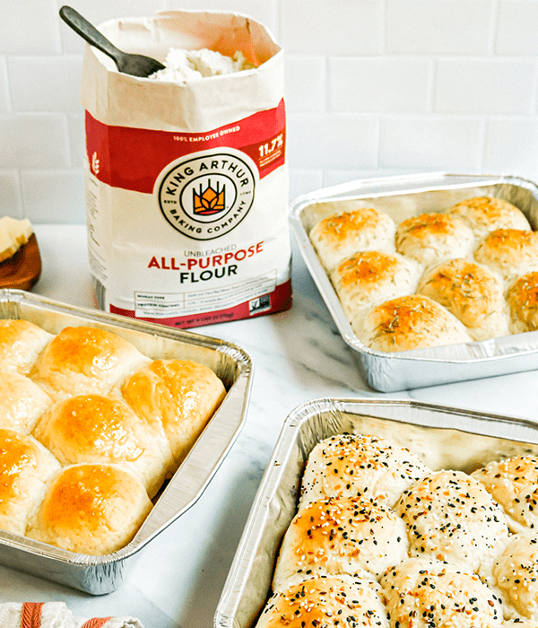 Three Pans filled with Fresh Baked Honey Butter Dinner Rolls, Garlic and Herb Dinner Rolls, and Everything Bagel Dinner Rolls with a bag of King Arthur Flour