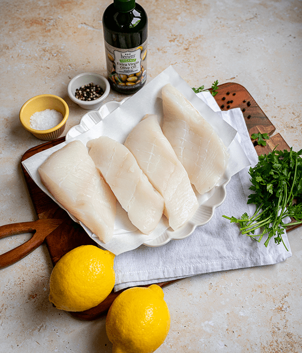 Fresh, Raw Halibut Fillets on a Plate Surrounded by Herbs, Spices, live Oil, and Lemons