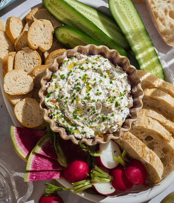 Smoked Trout Dip in a Serving Bowl Surrounded by Crostini Crackers, Baguette Slices, and Sliced Vegetables