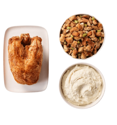 A Cooked Turkey Breast on a Plate with a Bowl of Stuffing and a Bowl of Mashed Potatoes
