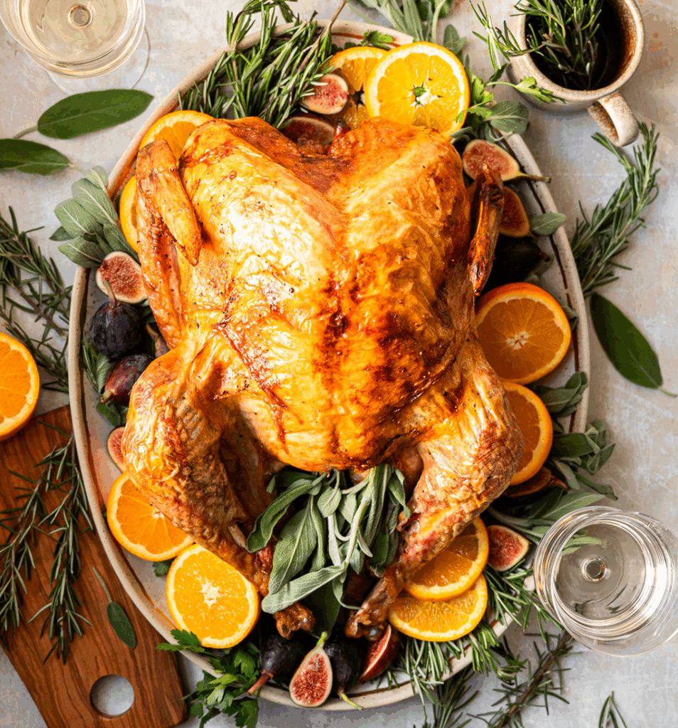 A Top-Down Image of a Cooked Whole Turkey on a Bed of Greens and Fresh Orange Slices